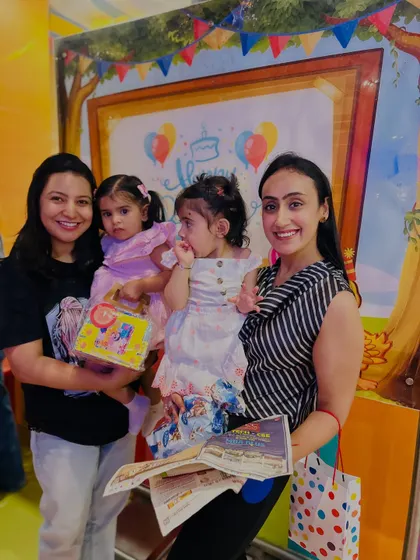 Mothers hold their toddlers and return gifts after a birthday party, a sweet conclusion to a joyful celebration.