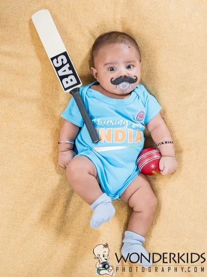 A future cricket star! This baby is dressed in a "Team India" onesie, complete with a mini bat, ball, and a playful mustache for a fun, sports-themed infant photo.