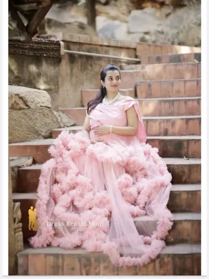 This shot on a staircase showcases the beautiful drape of the pink ruffled gown's train. It's a perfect setting to display the full volume and romantic texture of this rental dress.