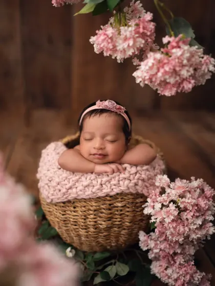 Surrounded by soft pink blossoms, this newborn girl is resting peacefully in a woven basket. This is a great example of a floral-themed newborn photoshoot.