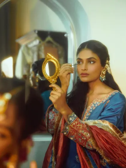 A storytelling moment from a campaign shoot. The model applying makeup in a vintage mirror creates a narrative of preparation and quiet beauty.