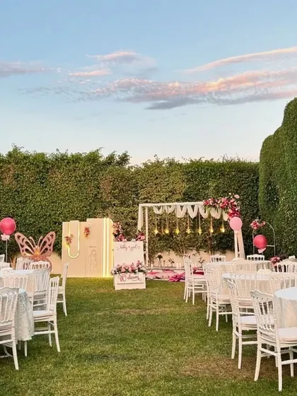 A beautiful outdoor sundowner setup for a 'Welcome Baby Girl' party, with elegant white tables, a low-seating area, and multiple themed photo backdrops.