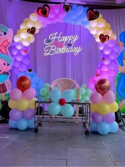 A fun Chhota Bheem themed birthday party. The setup includes a balloon arch with character cutouts on both sides and a 'Happy Birthday' neon sign.