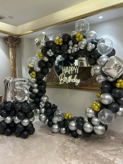 A 15th birthday party with a large circular balloon frame in black and silver. The setup includes a neon sign and a matching foil number balloon.