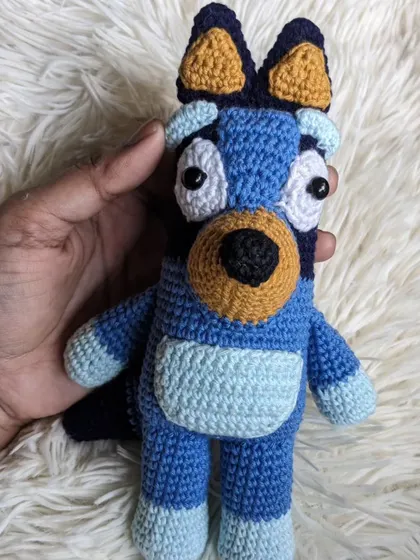 Holding the handmade Bluey toy, giving a clear view of its full body.