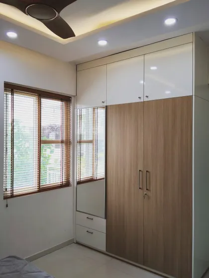 A simple and elegant wardrobe design that combines wood laminate doors with white overhead cabinets. The integrated mirror is a practical addition that also helps make the room feel larger.