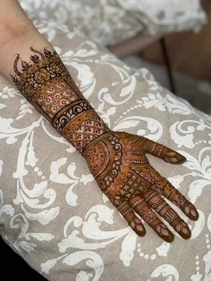 A full view of an intricate henna design on the front of the hand, extending up the forearm.