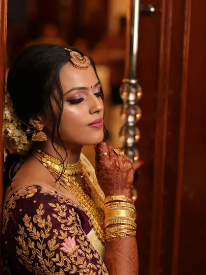A moment of quiet reflection for the bride. Her makeup is soft and romantic, with a focus on pink tones that complement her ornate blouse and jewelry.
