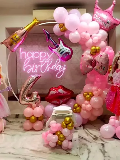 A glamorous Barbie theme for a 4th birthday. The decor is all about pink, with Barbie doll cutouts, a neon sign, and fun-shaped foil balloons like a guitar and lipstick.