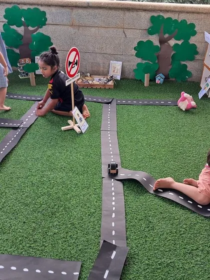 A wide view of the children fully engaged in playing with the miniature community. They are crawling, driving, and rearranging elements, taking full ownership of the space.