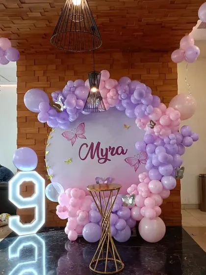 A beautiful butterfly-themed party for a 9th birthday. This setup features a circular backdrop with a pink and purple balloon arch and a large light-up number '9'.