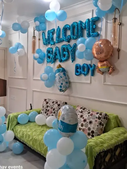 A full living room decoration to welcome a baby boy. The setup includes "WELCOME BABY BOY" foil balloons on the wall, balloon pillars, and loose balloons on the ceiling.