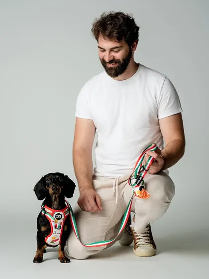 A full lifestyle shot of Riley the dachshund and his human, showing off the beautiful "Ciao Bella" collection from a local pet brand.