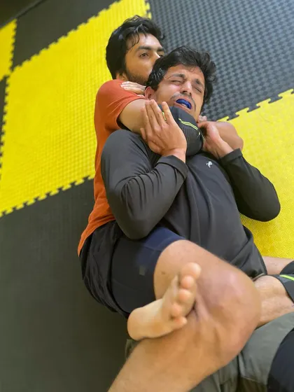 A close-up of a rear naked choke being applied. The mouthguard shows this is a live, intense roll.