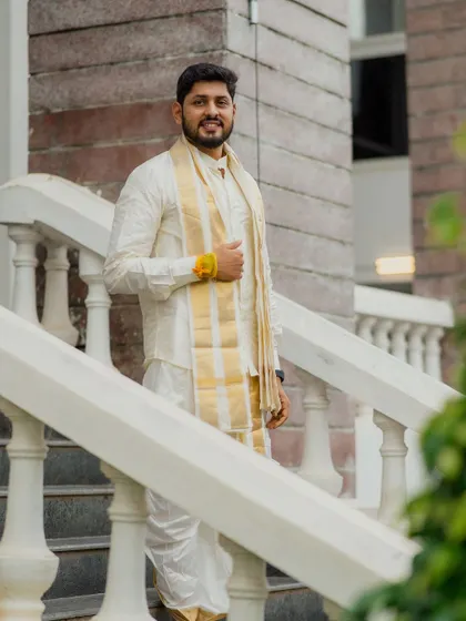 A handsome groom dressed in a traditional white and gold South Indian outfit. We make sure the groom's style and personality shine through in his portraits as well.
