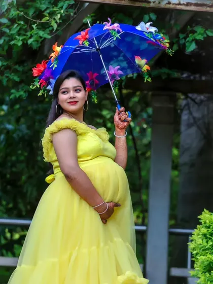 A bright and cheerful outdoor maternity shoot, with the expectant mother in a yellow ruffled gown holding a colorful floral umbrella.