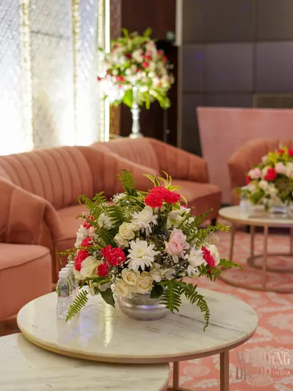 A floral arrangement on a marble-topped coffee table in a lounge area. The pink sofas in the background show how we coordinate our floral designs with the furniture and overall color scheme.