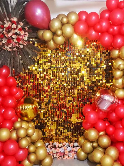 A glamorous photo backdrop for a party, featuring a gold sequin wall. The wall is framed by a vibrant arrangement of red and gold balloons, creating a perfect spot for pictures.