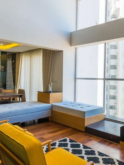 A sunlit duplex living area where modern yellow armchairs and a geometric rug add a playful touch, with large windows creating a bright and airy atmosphere perfect for relaxing.