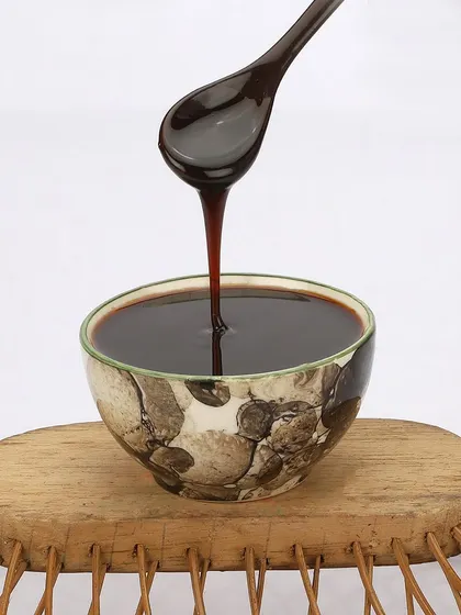 This action shot captures the thick, viscous texture of a food syrup as it's poured from a spoon into a bowl, ideal for highlighting product quality.