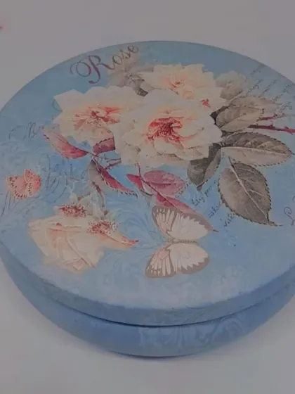 The lid of a vintage-style floral tin candle. The beautiful design means the container can be reused long after the candle is gone.