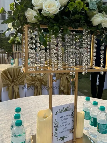 An elegant centerpiece at a floral-themed baby shower. A crystal-draped golden stand holds a beautiful arrangement of white roses, adding a touch of luxury to the table.