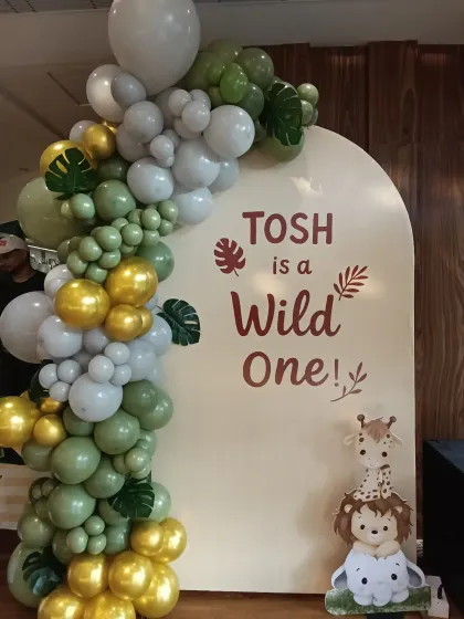 The 'Wild One' jungle theme is a huge hit for first birthdays. Here, I used an organic balloon arch in sage green, white, and gold around a custom arched panel, complete with cute jungle animal cutouts.