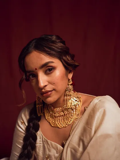 A stunning beauty shot focusing on the intricate gold jewelry. The warm lighting and the model's direct gaze highlight the craftsmanship and create a look of pure opulence.