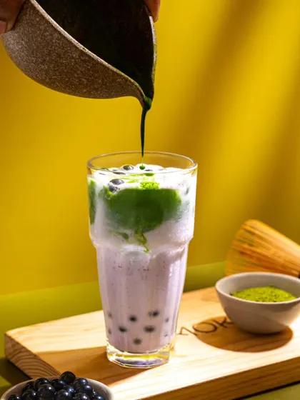Matcha being poured into a taro bubble tea. The color contrast and the action of the pour make for a dynamic and trendy beverage shot for Mokai.
