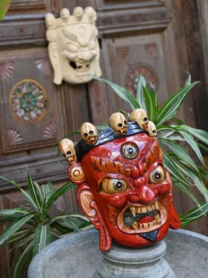 A red Bhairava mask and a white mask displayed together. The hand-carved wood is painted with natural colors to achieve the distinct emotions and characters that are central to Nepalese folk art.
