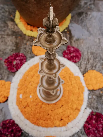 A traditional brass 'diya' or lamp, placed within a marigold rangoli. These elements are central to creating a sacred and auspicious ambiance for any ceremony.