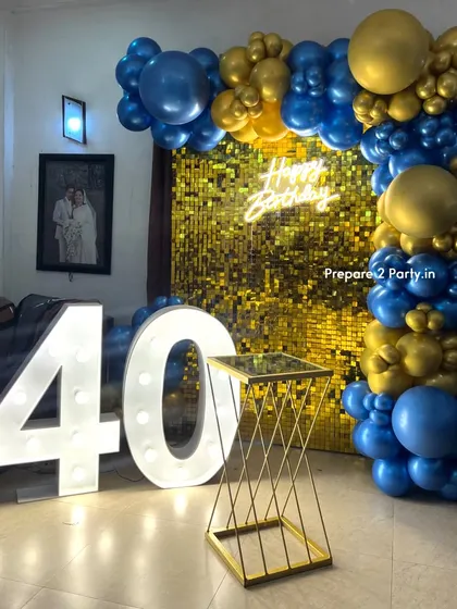 A classic and bold 40th birthday decoration for a home party. This setup features a gold shimmer wall, a neon sign, large marquee numbers, and a royal blue and gold balloon frame.