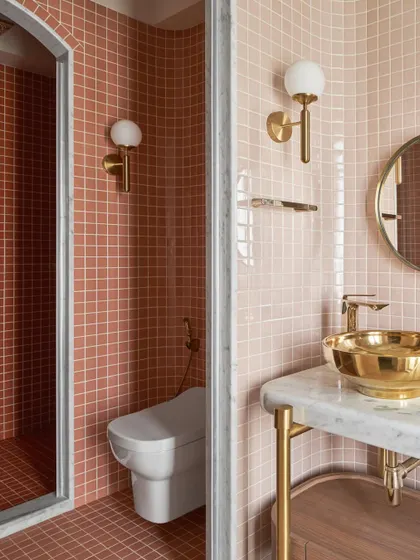 A detail of the kid's bathroom, showing the gradient of pink tiles in the shower area. The brass fixtures and globe sconces add a touch of warmth and glamour to the space.