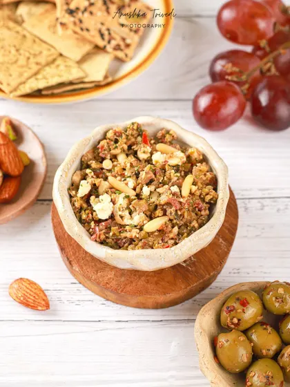 A rustic bowl of olive and nut tapenade, styled with crackers and grapes for a perfect appetizer spread.