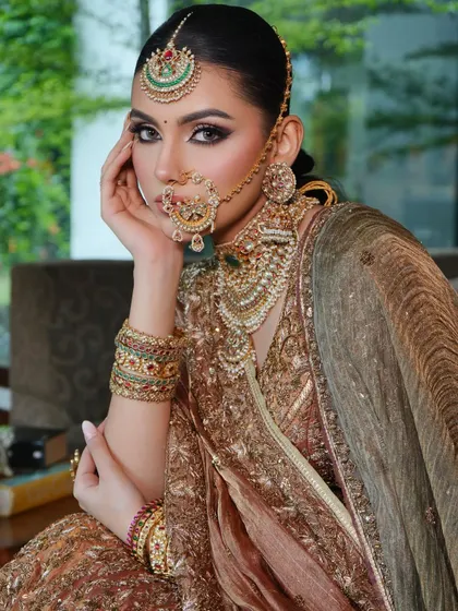 A close-up on bridal beauty. This shot highlights the detailed makeup and the magnificent traditional jewelry, including a maang tikka, nath, and layered necklaces, that complete this opulent bridal look.