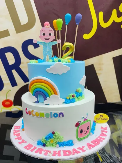 A vibrant two-tiered Cocomelon cake for a second birthday. This 3kg cake is decorated with a rainbow, clouds, and beloved characters from the show.