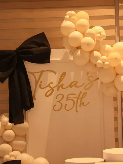 A detail shot of the custom gold lettering and large black bow on the birthday backdrop.