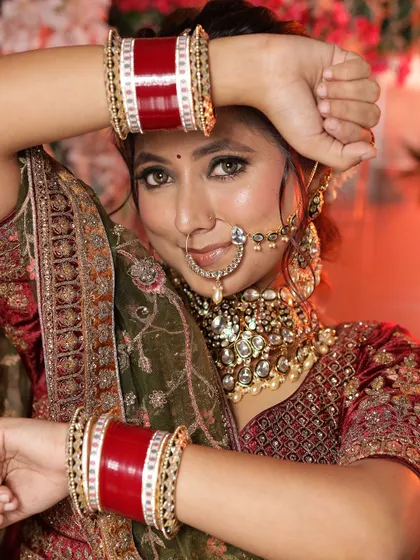 A close-up on the bride's hands, showcasing her chooda (bridal bangles) and the intricate embroidery of the lehenga.