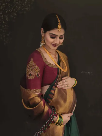 A close-up focusing on the tender connection between mother and baby. Her gentle touch on the bump, combined with the rich textures of the silk saree, makes for a deeply emotional and artistic portrait.