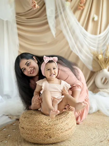 A mother and daughter share a happy moment on a woven pouf. The baby's bright smile and the mother's loving expression make this a delightful portrait.