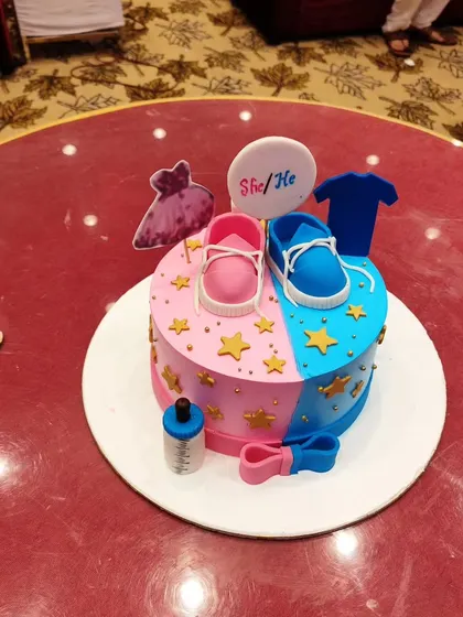 A classic 'She or He' gender reveal cake, perfectly decorated with pink and blue shoes, a dress, and a t-shirt. It’s a sweet centerpiece for the celebration.