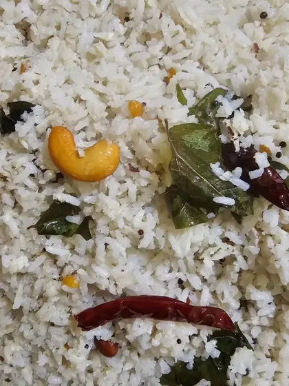 A close-up of a seasoned rice dish, possibly a lemon rice or coconut rice, tempered with cashews, curry leaves, and red chilies.