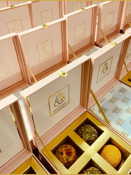 We specialize in personalized wedding gifts. These elegant pink and gold boxes feature a custom monogram for the couple, filled with delicious laddus for a sweet beginning.