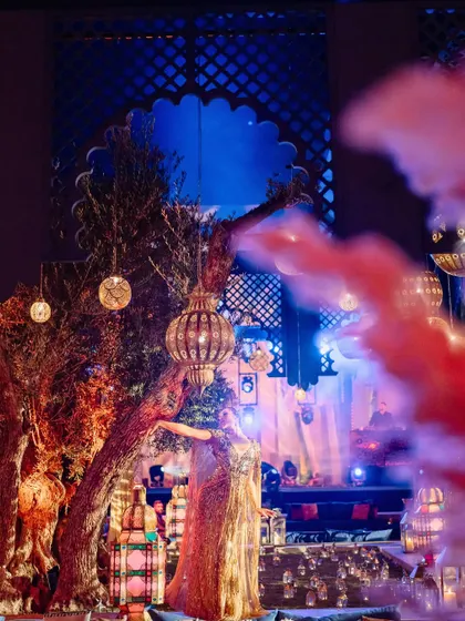 A performer dances amidst ancient olive trees decorated with hanging lanterns, blending entertainment with the natural beauty of the venue.