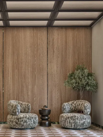 A waiting area should feel like a comfortable pause. We used plush, sculptural armchairs against a warm wood-paneled wall and an olive tree to create a calm and inviting seating nook in this office lobby.