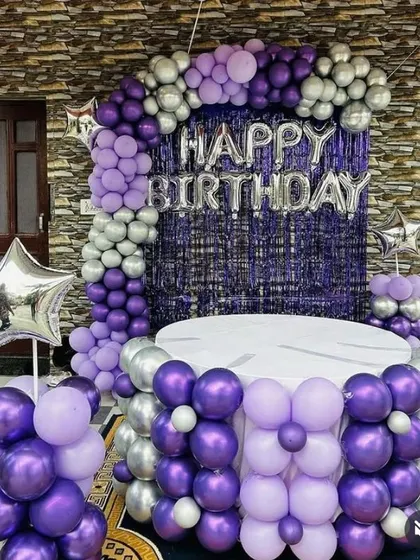 A purple and silver balloon decoration with a fringe backdrop and a balloon-covered cake table.