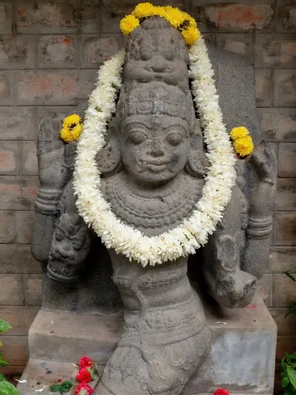 A stone statue at the venue, adorned with a simple floral garland, integrating the decor with the location's soul.