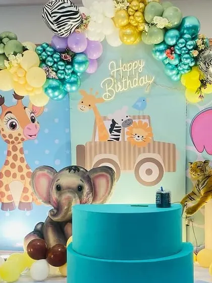 A cute Jungle theme party with cartoon animal cutouts like a giraffe and elephant, set against a custom backdrop and a green and yellow balloon arch.