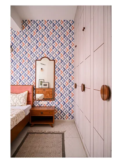We used a bold, geometric wallpaper in this bedroom to create a vibrant and energetic feel. A peach-upholstered bed and a simple grey wardrobe with circular wooden handles balance the drama of the pattern.
