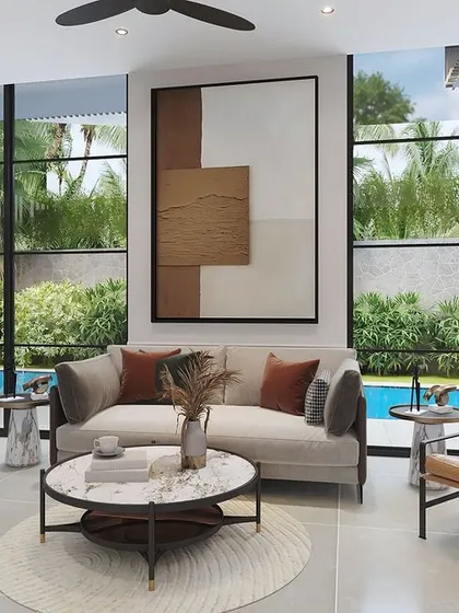 The living room of a Goa villa, where large windows frame the lush tropical garden and pool. The interior is minimalist yet warm, with comfortable seating and abstract art creating a sophisticated coastal atmosphere.